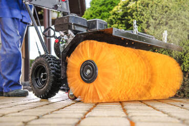 Commercial pressure washing machine with orange scrub brush cleaning block walkway.