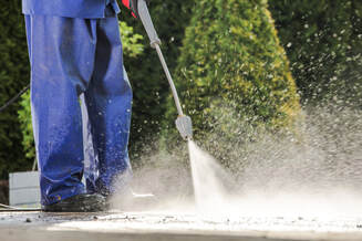 Pressure washing dirty walkway. Worker wearing blue pants