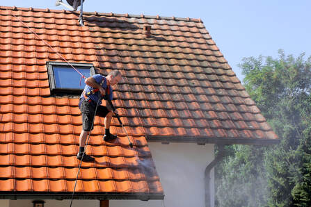Technician powerwashing an orange tile roof with skylight. Half is cleanded